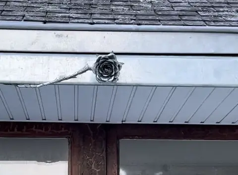 La rose en zinc et sa tige soudées sur le bandeau de la lucarne rénovée, au-dessus de la fenêtre à cadre bois