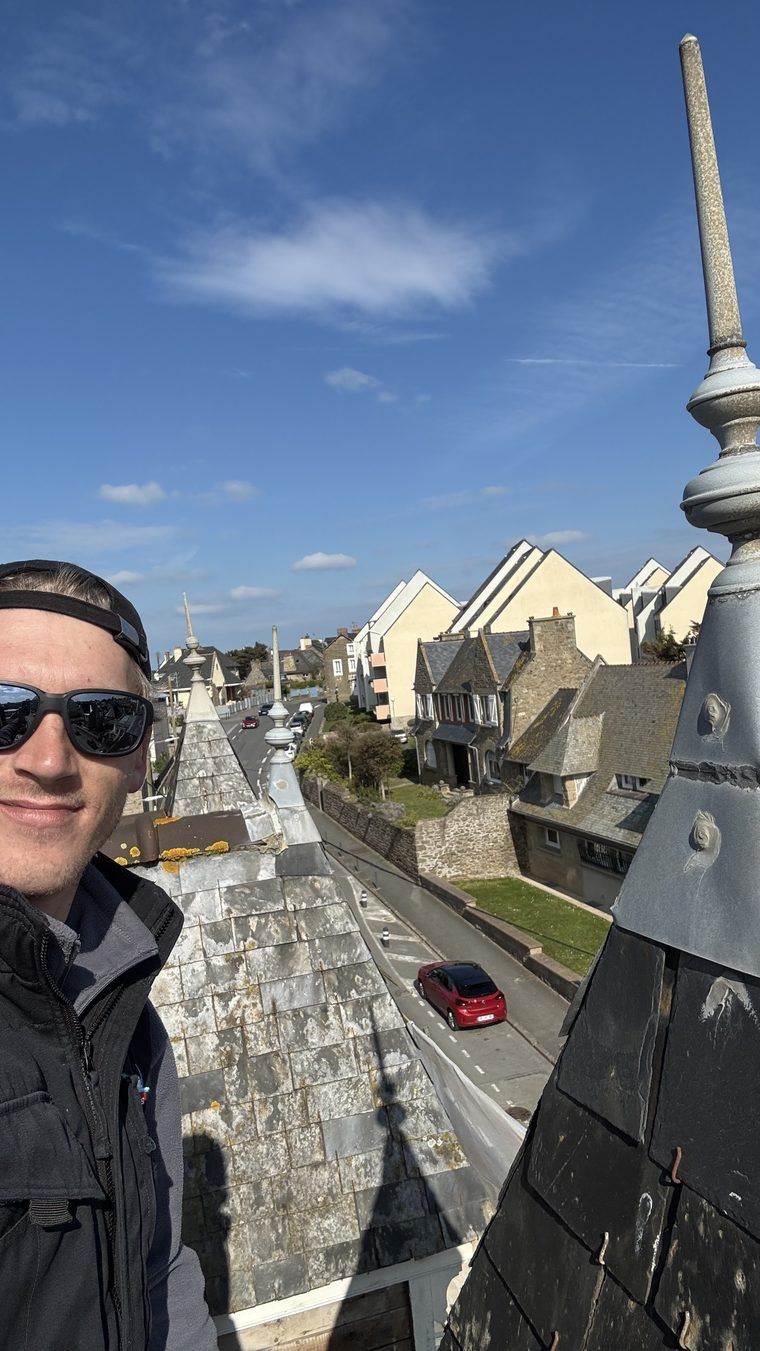 Couvreur au faîtage d'une tourelle en ardoise, épis de faîtage en zinc, rue de villas en contrebas