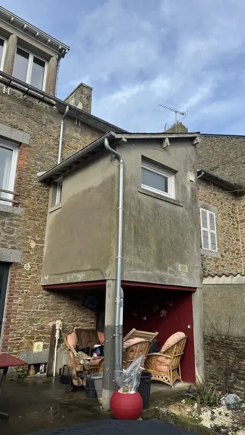 Extension en encorbellement avant travaux à Cancale : enduit gris fissuré et taché par les ruissellements, adossée à une maison en pierre