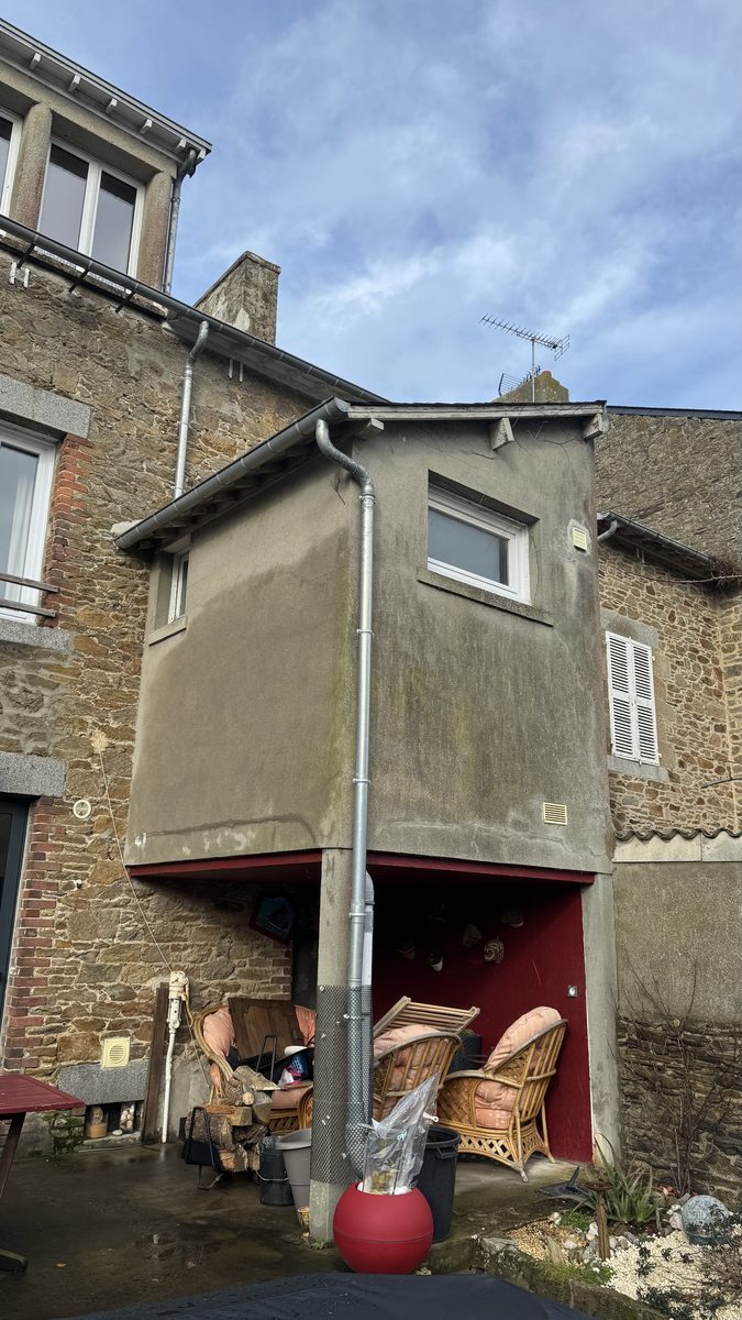 Extension en encorbellement avant travaux à Cancale : enduit gris fissuré et taché par les ruissellements, adossée à une maison en pierre