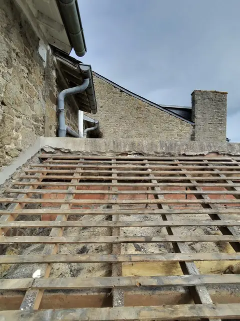 Ancienne couverture déposée : liteaux et remplissage mis à nu au pied du pignon en pierre, souche de cheminée en arrière-plan