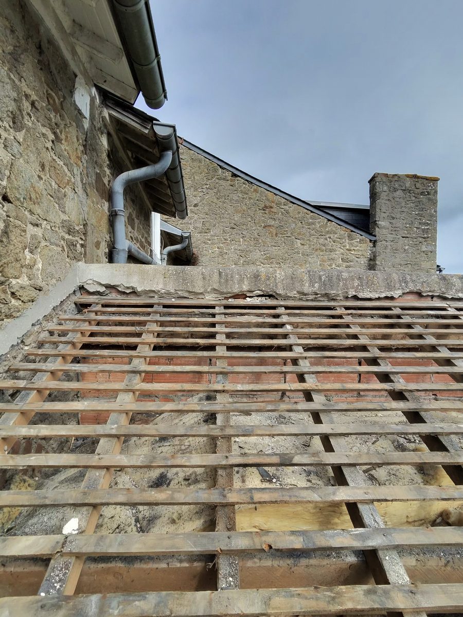 Ancienne couverture déposée : liteaux et remplissage mis à nu au pied du pignon en pierre, souche de cheminée en arrière-plan