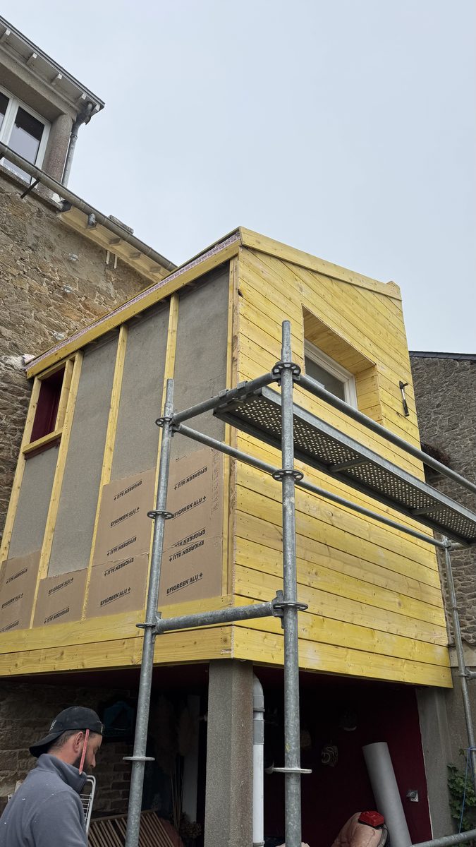 Ossature bois et panneaux isolants rigides à parement aluminium sur les façades de l'extension, voligeage déjà posé sur le pignon