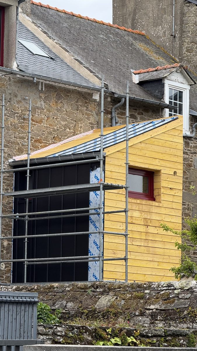 Vue depuis la rue à Cancale : façade en zinc anthracite terminée, toiture monopente en zinc en cours de pose, bardage bois en attente