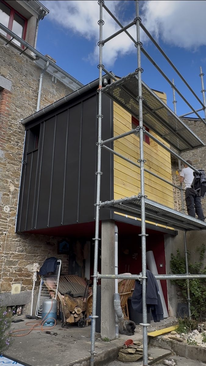 Façade et sous-face en zinc anthracite terminées, dernier pignon en bois en cours d'habillage par un couvreur sur l'échafaudage
