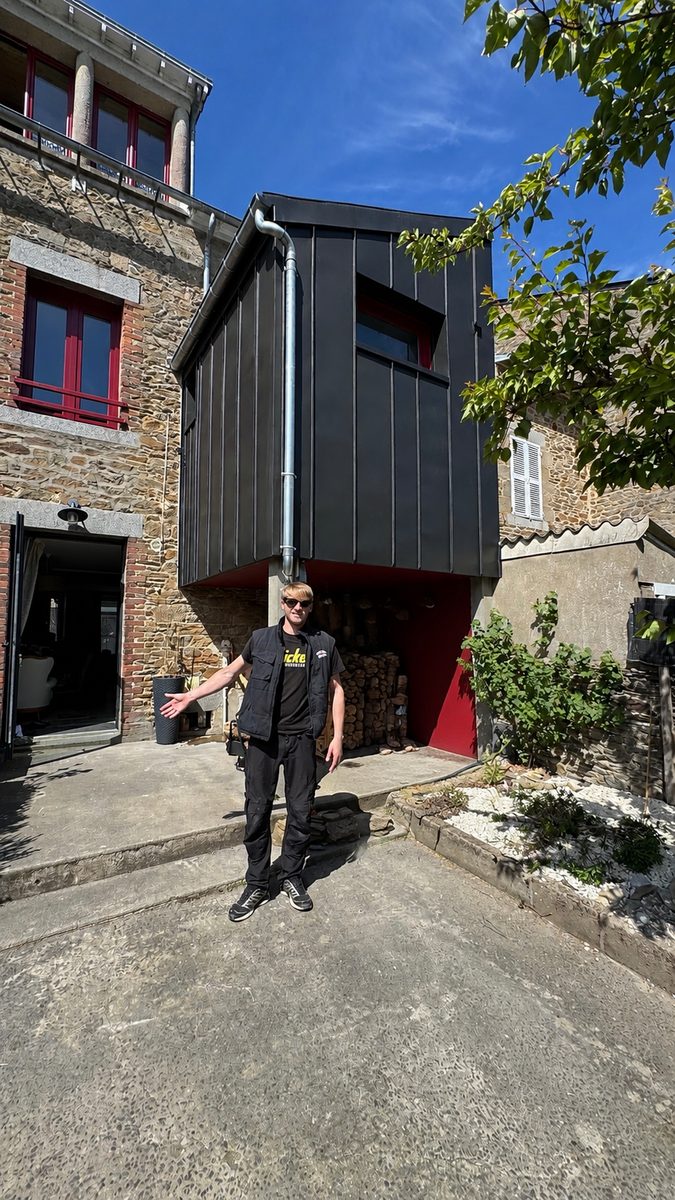 Willy Lambert présentant l'extension terminée à Cancale, entièrement habillée de zinc anthracite à joint debout, dans la cour de la maison en pierre