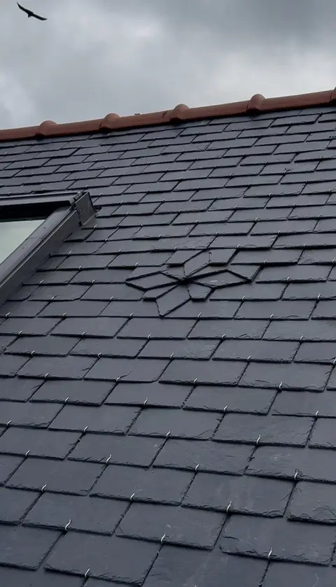 Rosace découpée dans l'ardoise d'une toiture neuve, à côté d'une fenêtre de toit, faîtage en tuiles