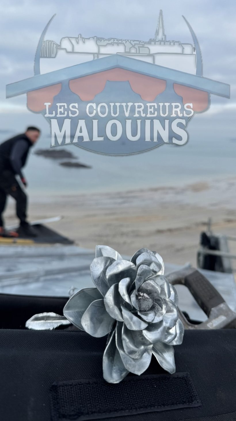 Rose en zinc façonnée à la main posée sur un chantier face à la plage de Saint-Malo, couvreur au travail en arrière-plan
