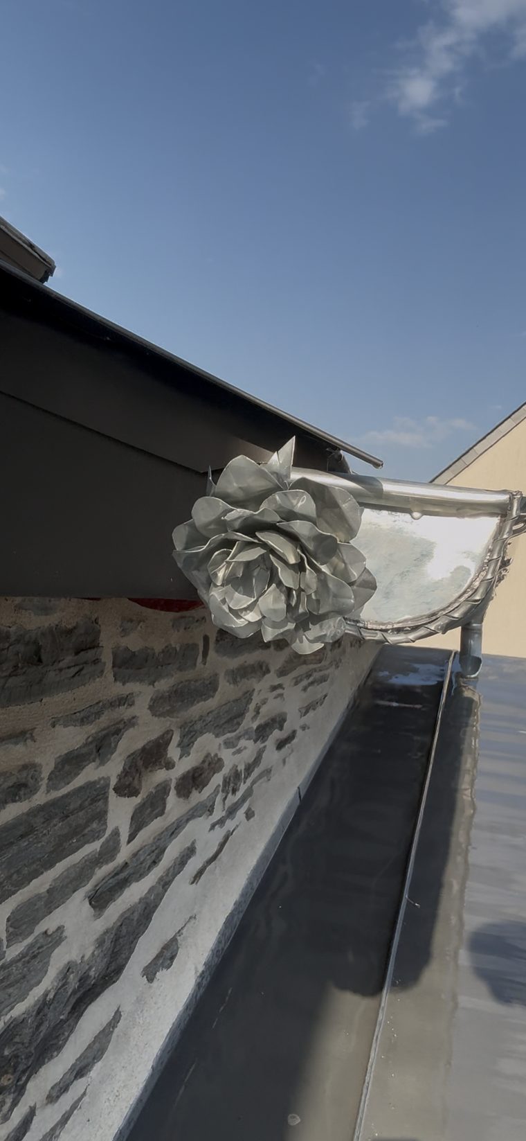 Gros plan sur une rose en zinc aux pétales façonnés à la main, soudée sur la naissance d'une gouttière