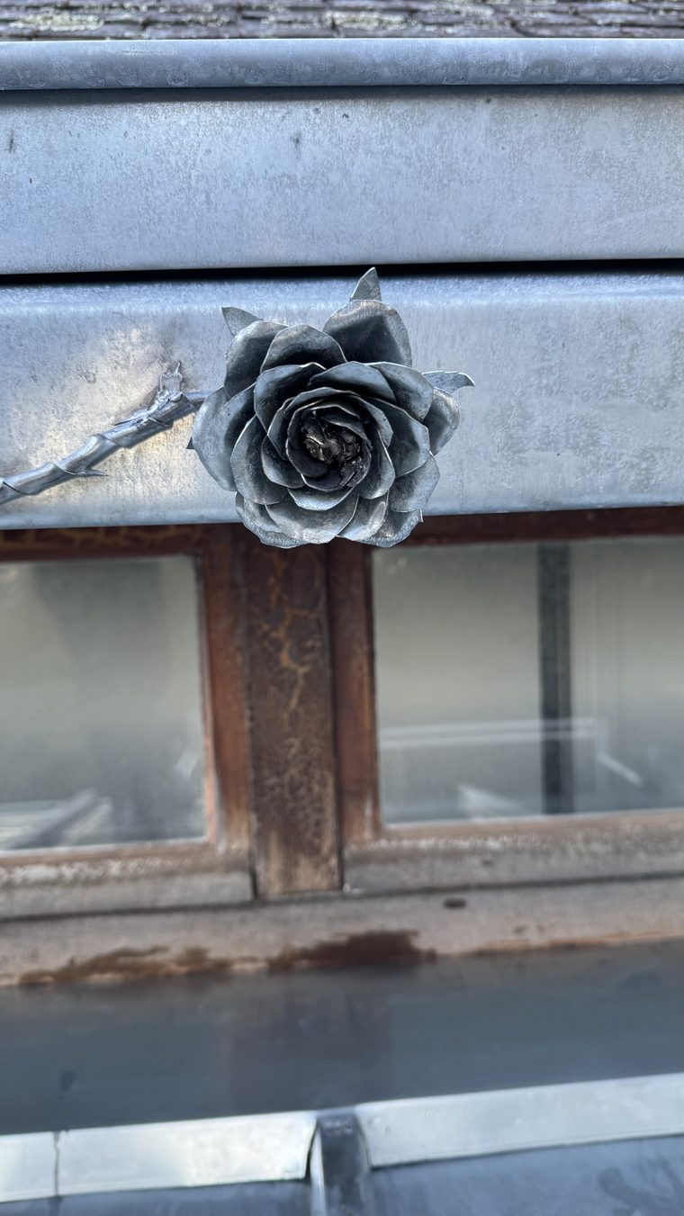 Gros plan sur une rose en zinc soudée sur le bandeau d'une lucarne, pétales façonnés à la main