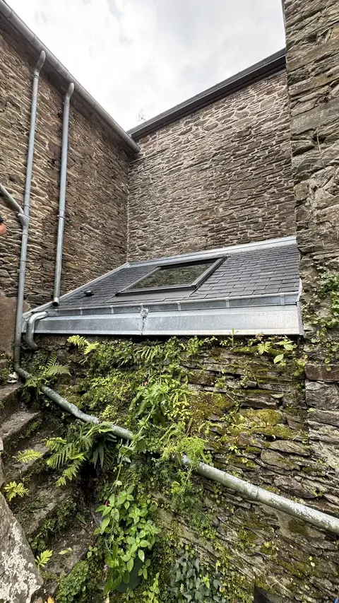 Vue d'ensemble depuis la cour : nouvelle lucarne en ardoise avec fenêtre de toit, bandeau et gouttière zinc, entre les murs de pierre