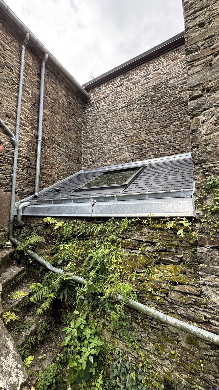 Vue d'ensemble depuis la cour : nouvelle lucarne en ardoise avec fenêtre de toit, bandeau et gouttière zinc, entre les murs de pierre