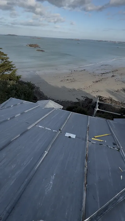 Ancien zinc du terrasson en fin de vie : couvre-joints fendus, rustines et feuilles fissurées, vue plongeante sur la plage