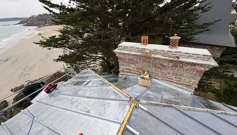 Pose du zinc neuf à tasseaux sur le terrasson, au pied de la souche de cheminée en brique et granit, plage de Saint-Lunaire en contrebas