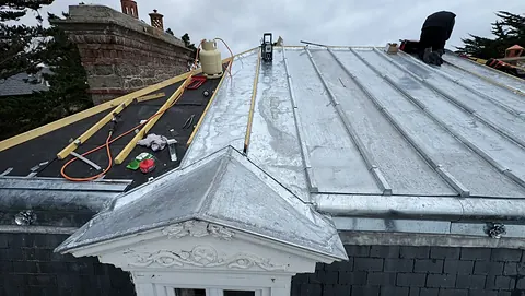 Fronton de lucarne habillé de zinc, terrasson à tasseaux en cours, écran et tasseaux sur le pan voisin, membron orné de roses en zinc