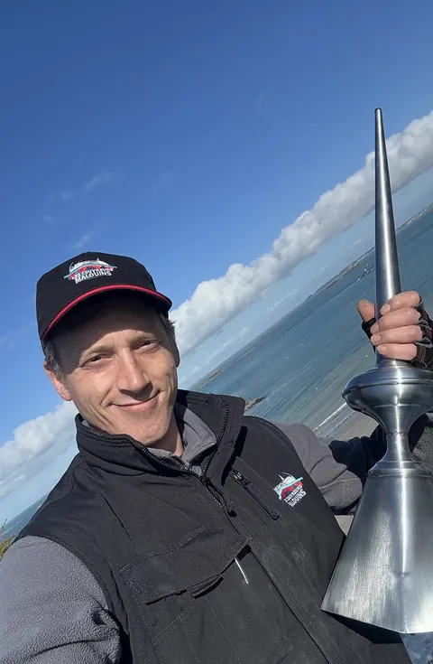 Couvreur sur le toit tenant l'épi de faîtage en zinc, la mer et les îlots de Saint-Lunaire en arrière-plan