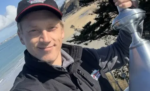 Willy Lambert présentant un épi de faîtage en zinc poli devant la plage de Saint-Lunaire, avant sa fixation sur la villa